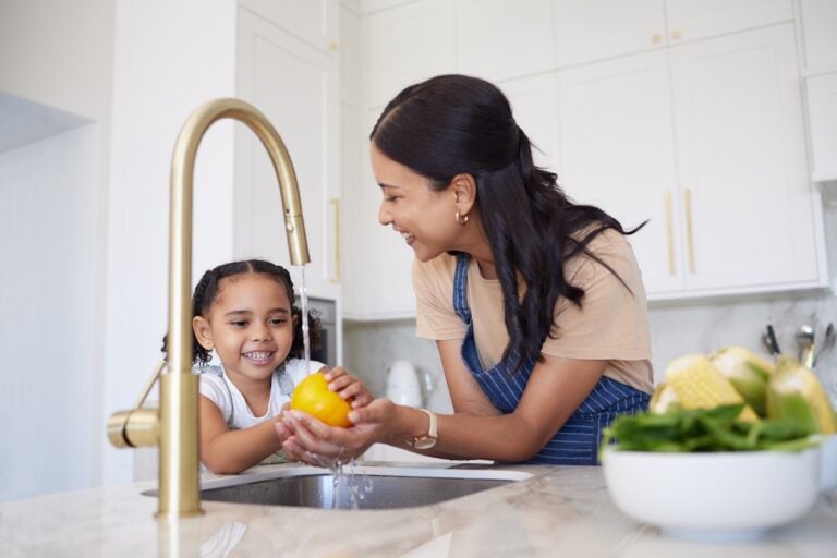 Vegetable, family and washing with a girl and mother cleaning a pepper in the kitchen of the home together for hygiene. Kids, health and cooking with a woman and daughter using a basin to rinse food.