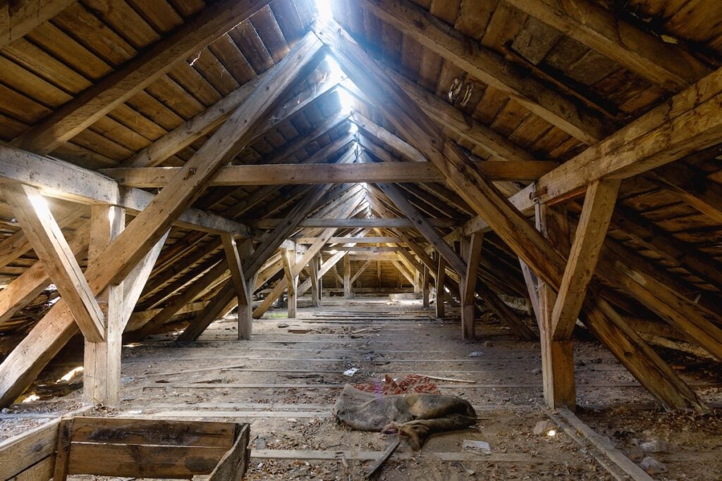 The attic of an old ruined house, light shines through holes in the roof
