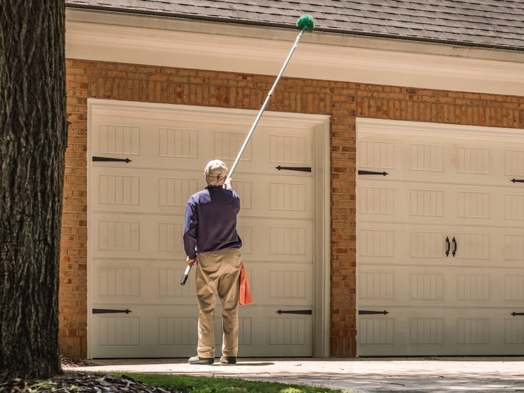 Man cleaning gutters of the house with a long handle broom brush